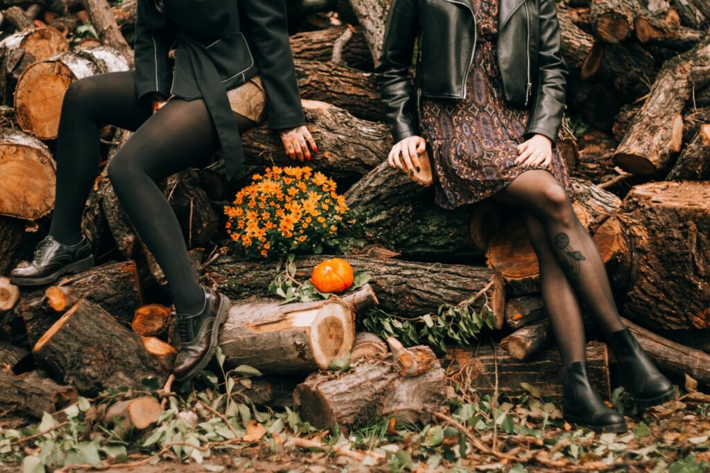 Women in autumn attire sitting on tree logs with pumpkins and flowers.